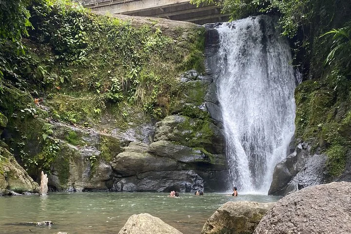 Des personnes nagent dans une piscine au pied d'une magnifique cascade.